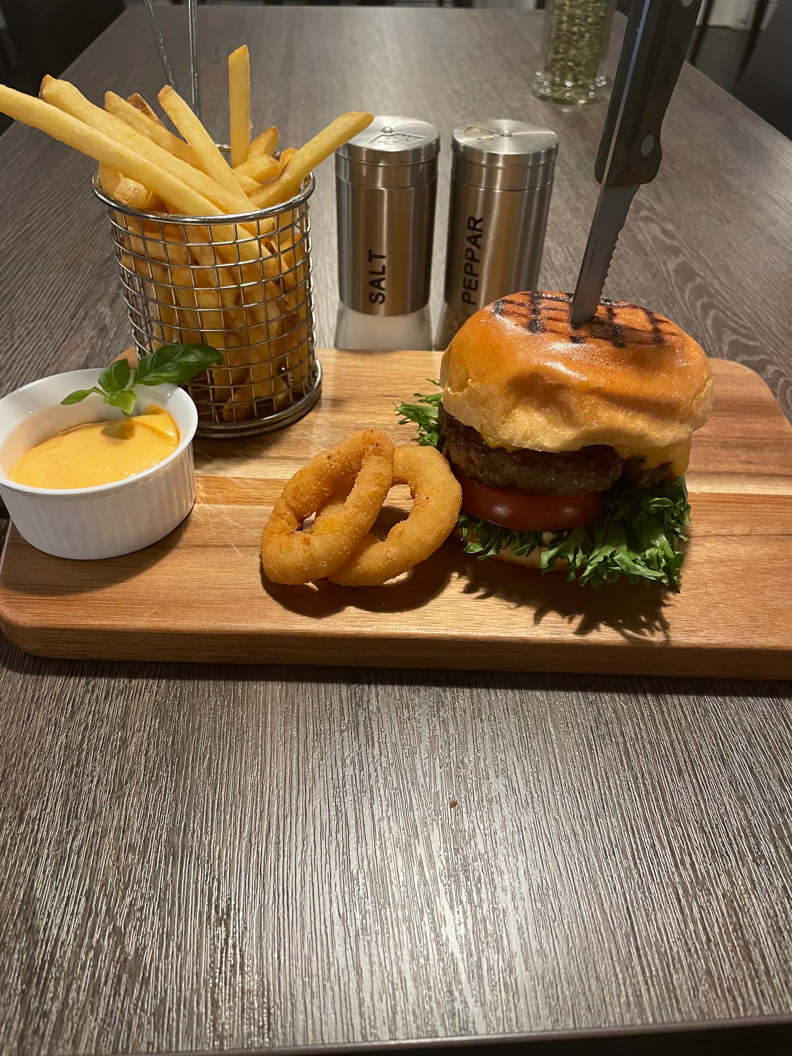 Hamburgare med pommes frites, lökringar och dippsås serverad på träbricka