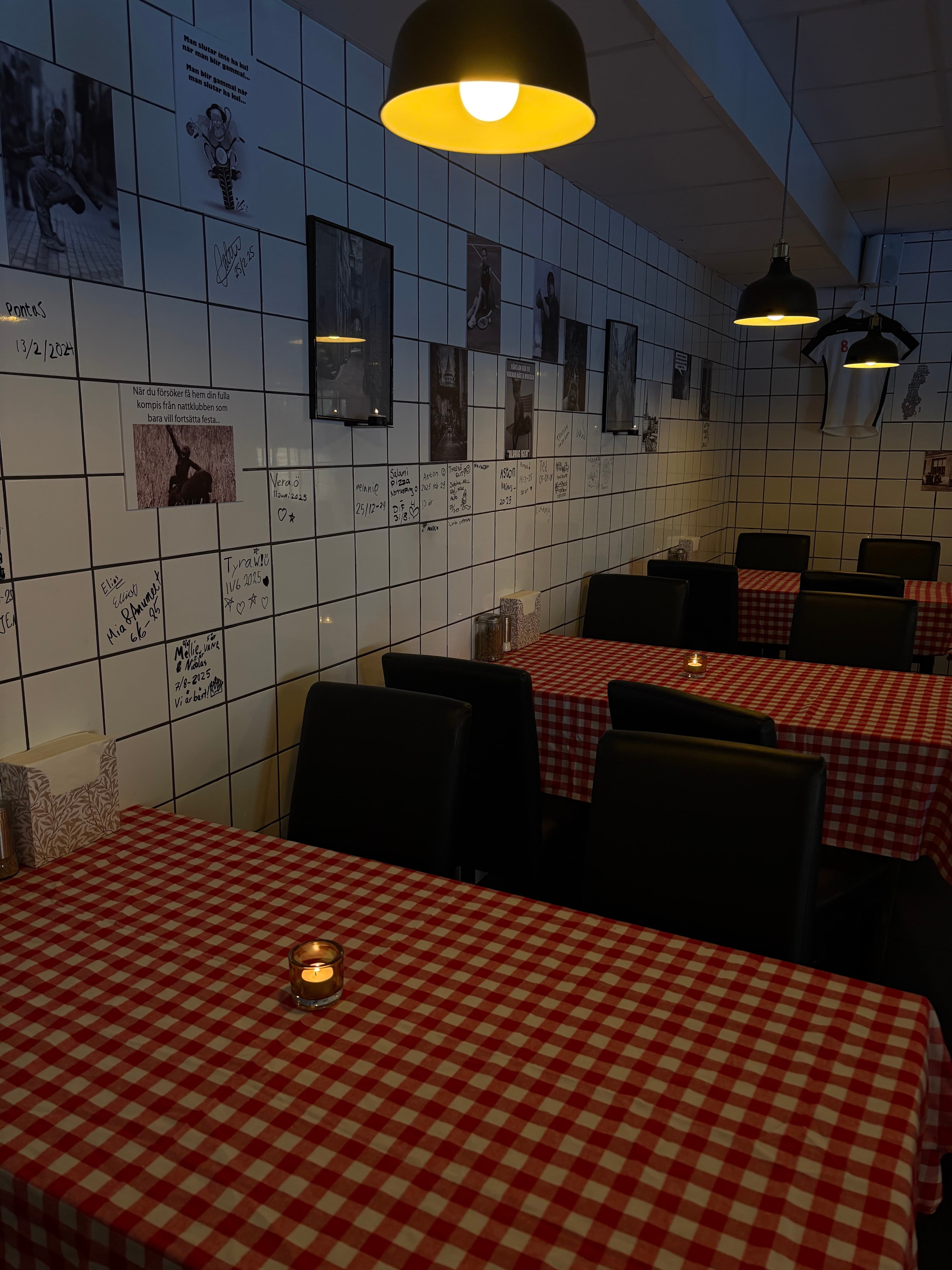 Matsal med rödrutiga dukar, minnesvägg och varm belysning