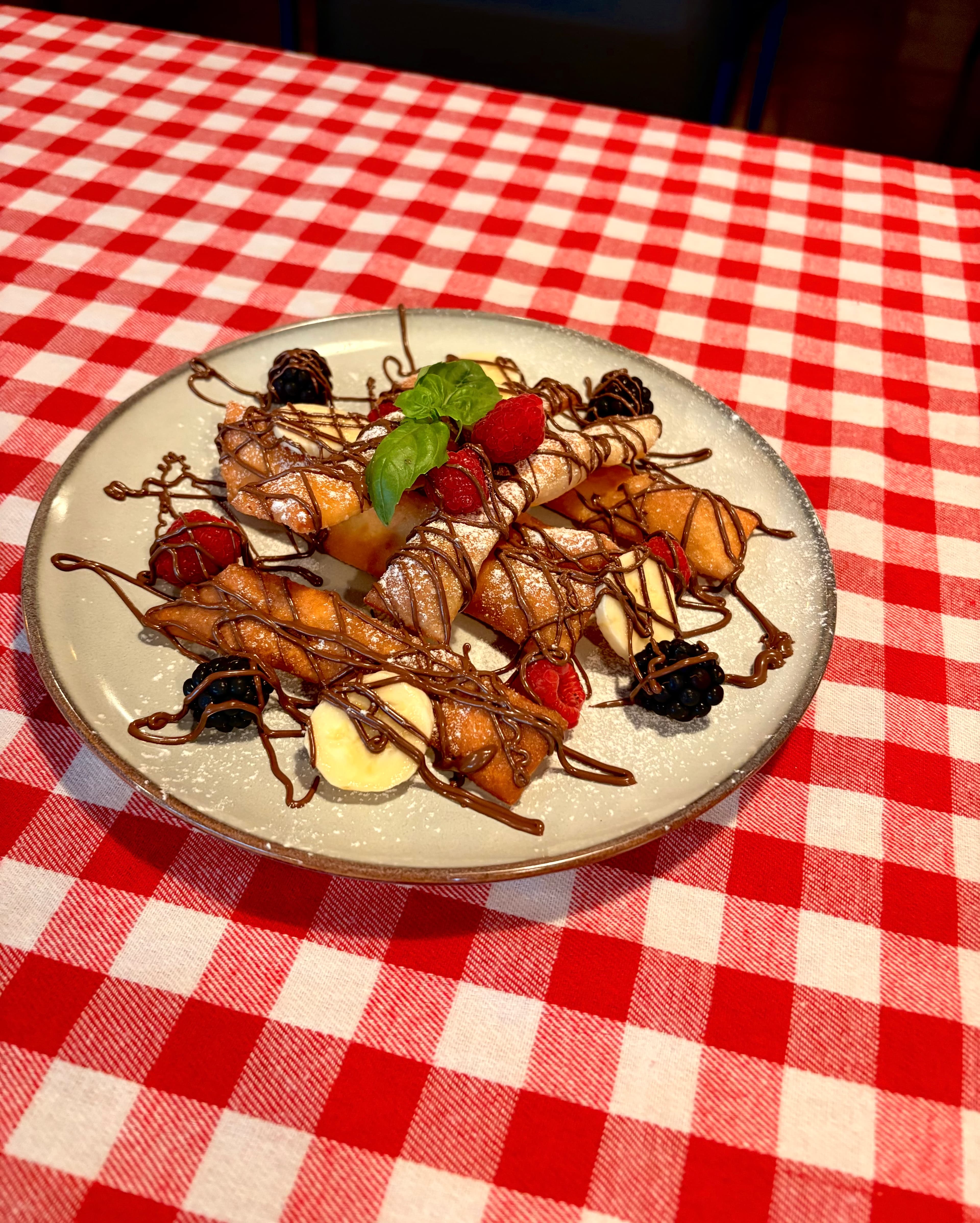 Dessert med friterad deg, choklad, bär och banan på rödrutig duk